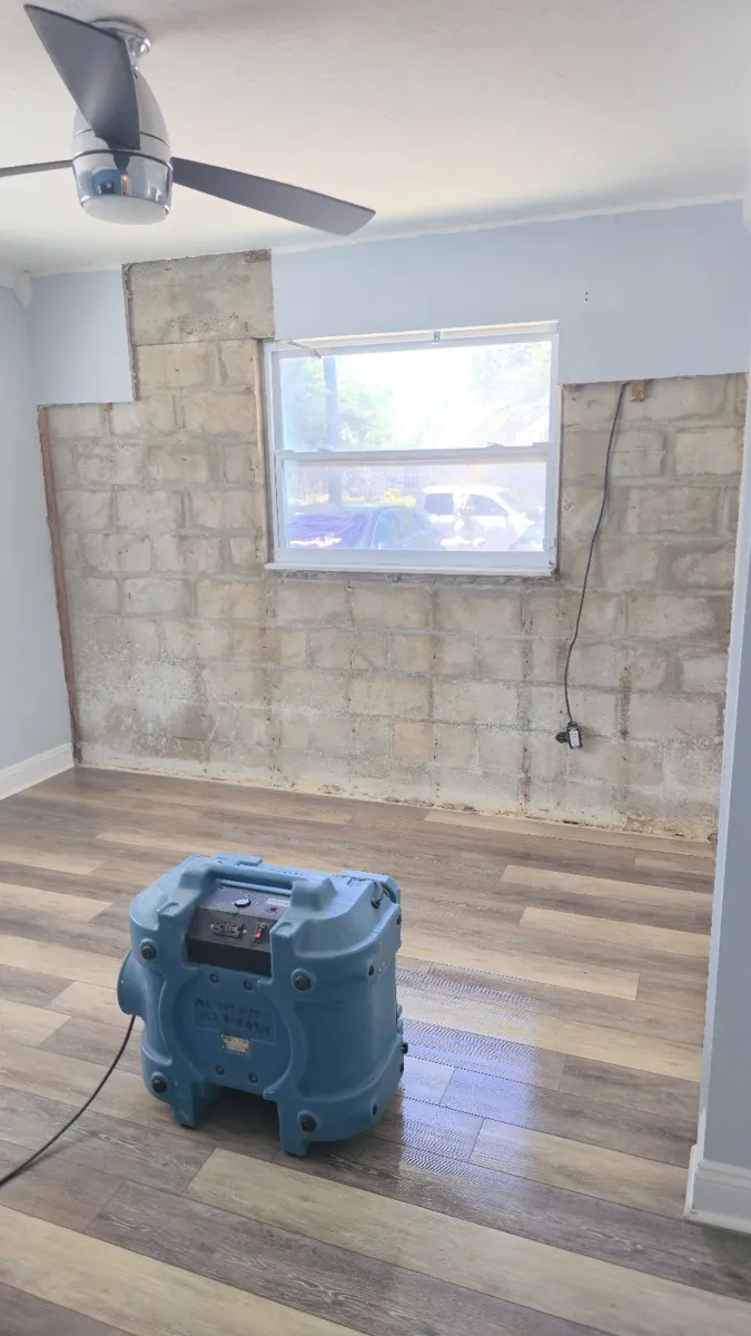 Air mover drying a laminate floor beside a water-stained wall