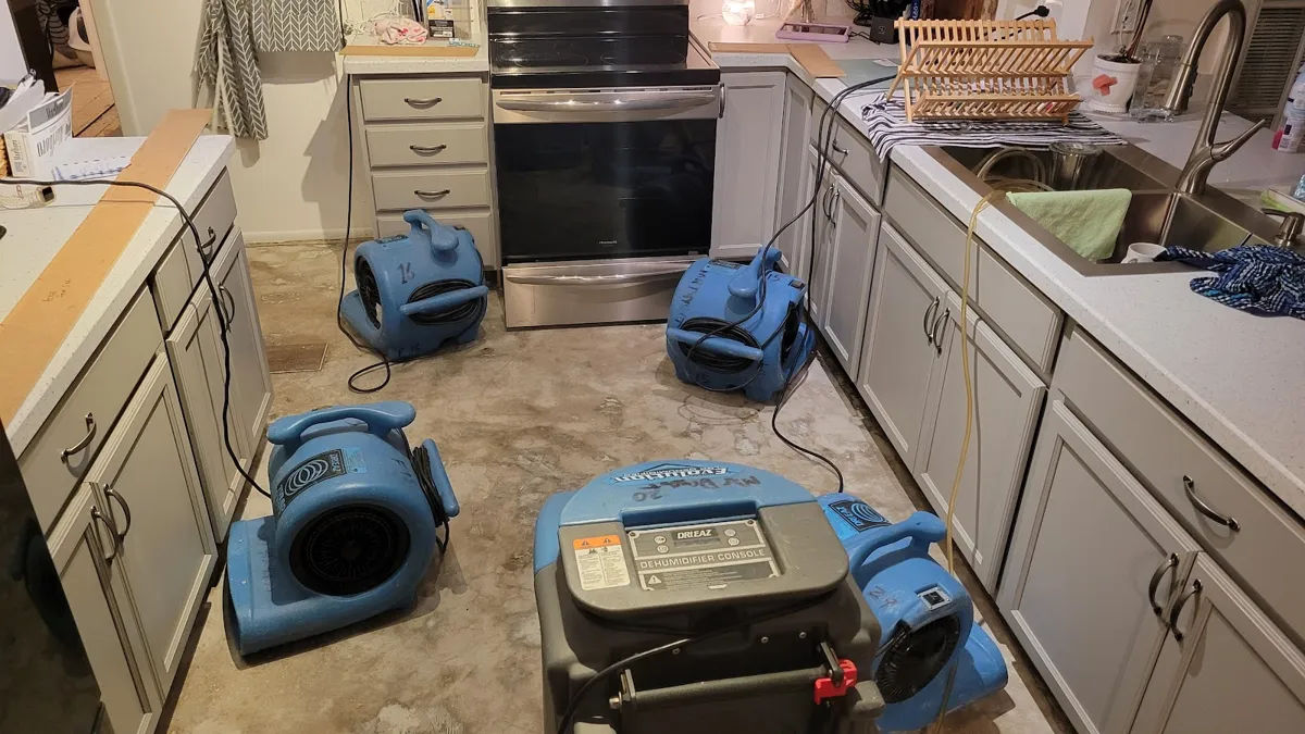 Air movers and a dehumidifier drying a kitchen floor and cabinets