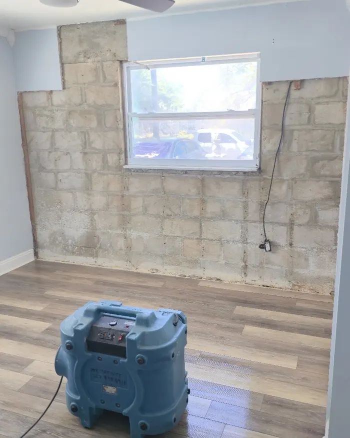 Room with the lower drywall removed down to the concrete block wall and drying equipment running on the floor