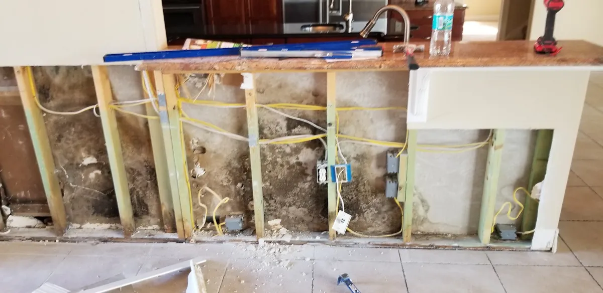 Kitchen wall opened up with the wet drywall cut out above the cabinets
